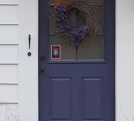 A NoKnock decal in place on a front door, at eye level beside the handle